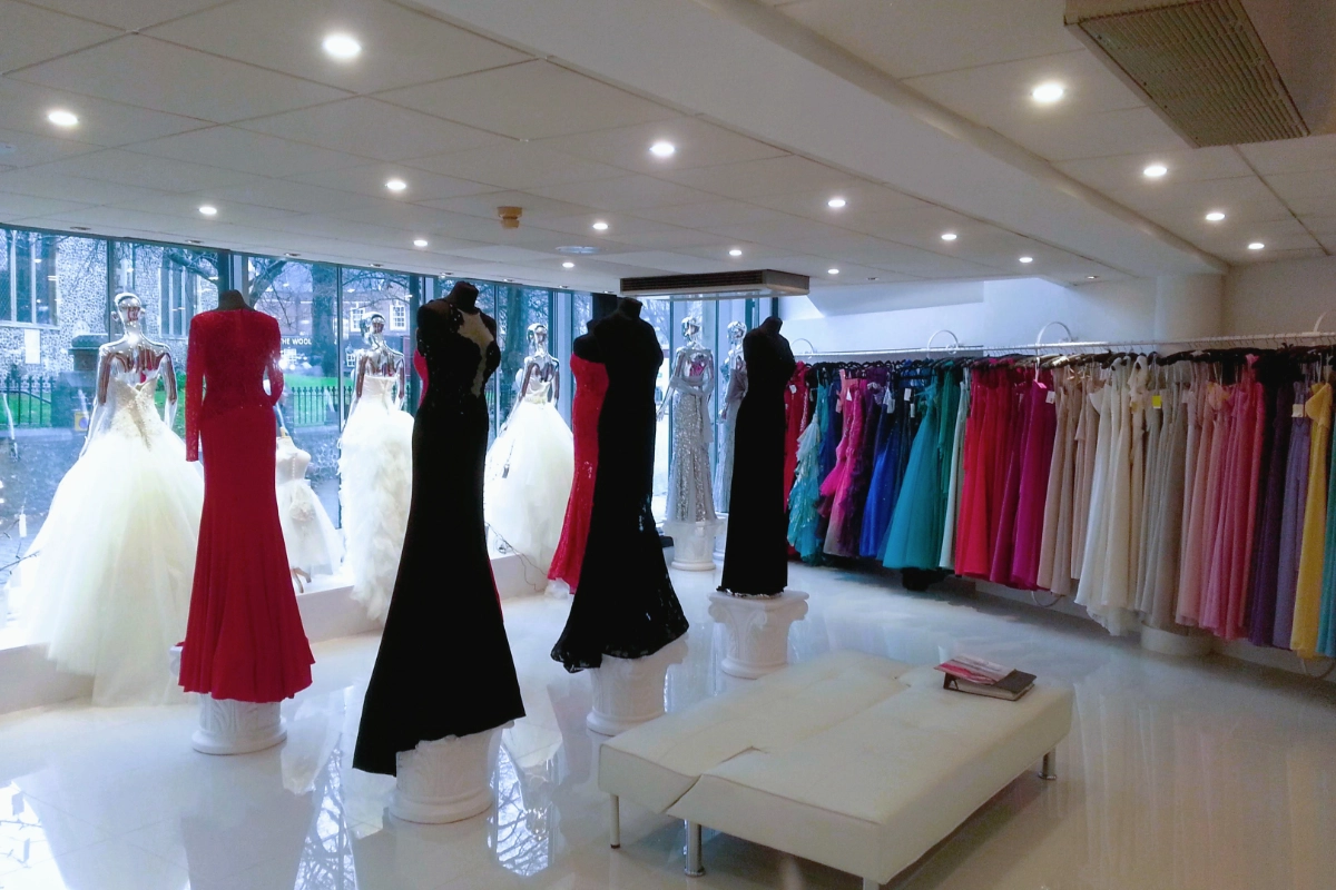 Brightly lit bridal and formalwear boutique with ceiling spotlights illuminating dresses and mannequins.