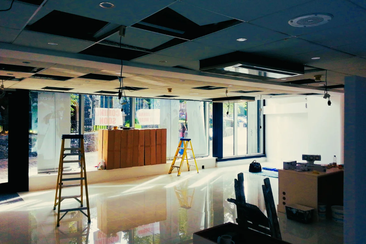 Commercial retail interior undergoing electrical and ceiling installation work with ladders and exposed fittings.