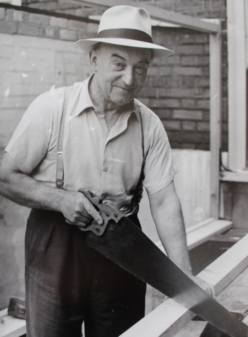 Herbert Noble wearing a hat and holding a hand saw