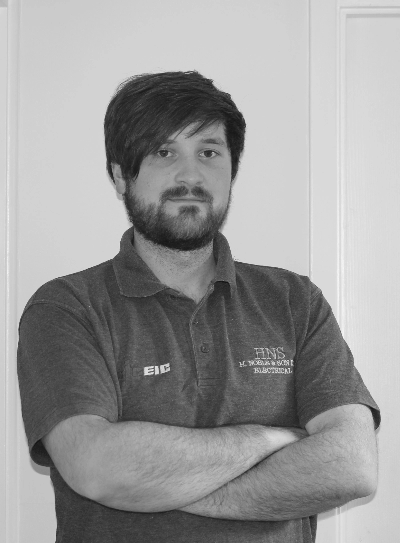 Black-and-white portrait of a bearded man standing with his arms crossed