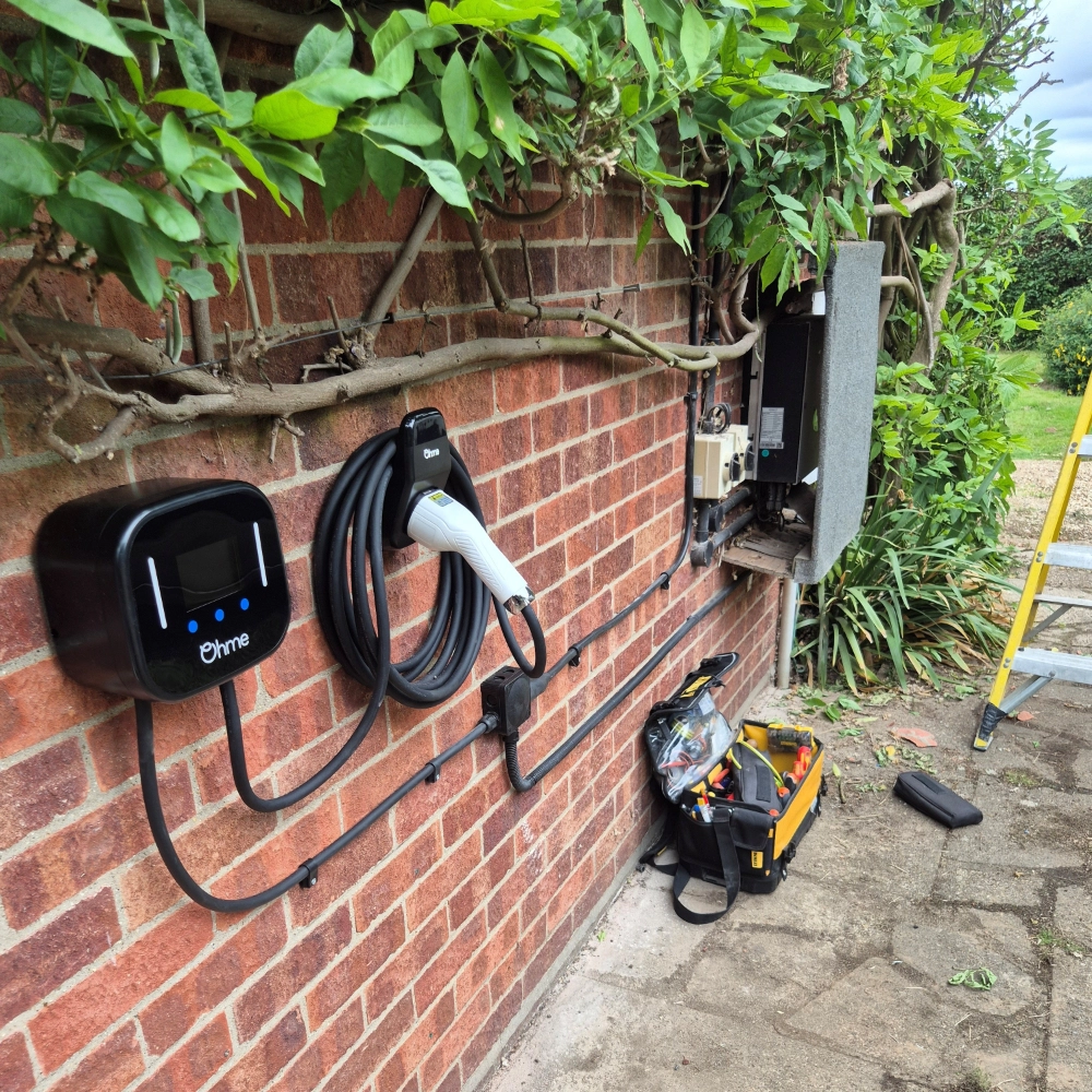 Ohme home EV charger mounted on a brick wall during installation, with electrical tools and equipment nearby.